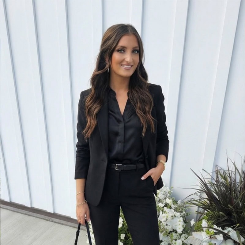 Chic woman in black suit with floral backdrop for wedding occasions | Timeless Celebrations.